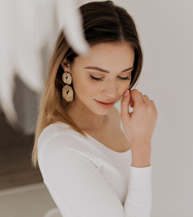 pretty-tenseness-woman-with-nude-make-up-wearing-golden-earrings-is-touching-her-cheek-smiling-with-closed-eyes-isolated-background